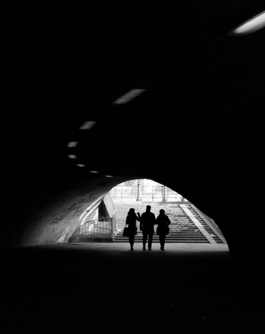 A group of three shadowy figures walk away from our view in a dark underground tunnel like you see in so many urban or metro parks. Looks like they're talking as a team as they leave anonymously. If we had to guess, they look like private intelligence consultants or spies.
