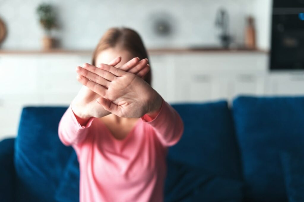 An anonymous woman wearing a pink shirt has her hands in front of her face in a crossed or "x" pattern. She is doing this to conceal her identity from the vantage point we're facing her. Online privacy is becoming harder and harder to achieve, which is why we share best practices to help you!