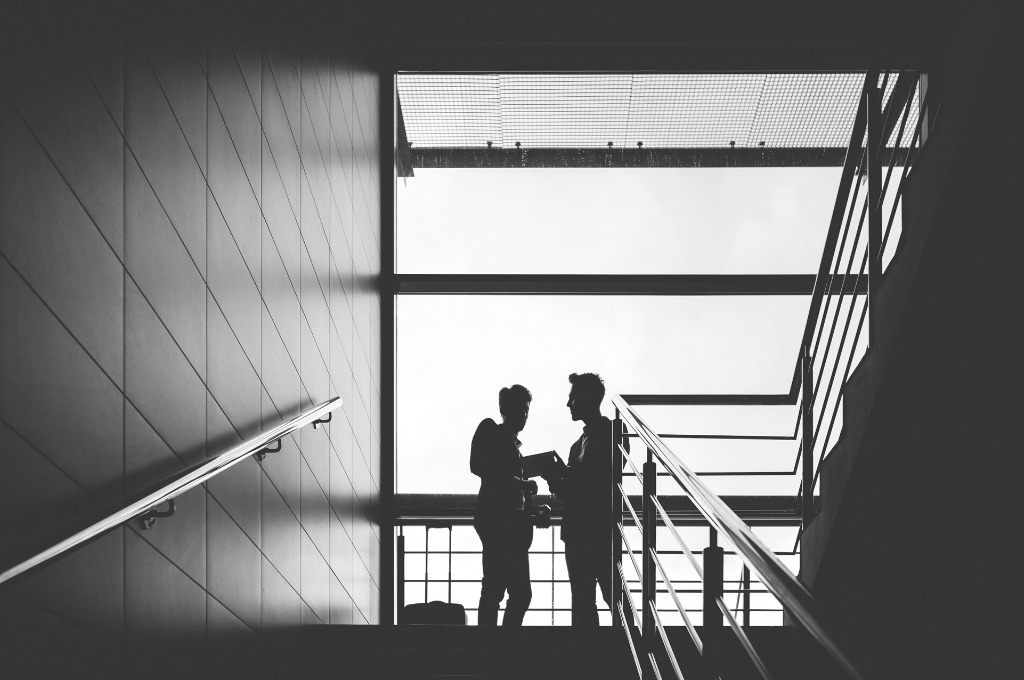 Two people are talking privately and somewhat discreetly in a large corporate office complex's stairwell. When performing Human Intelligence collection (HUMINT) it's imperative to develop warm relationships with key personnel easily.