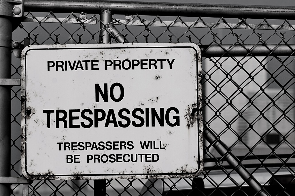 A No Trespassing sign on a chain link fence outside of some sort of facility. Reveille Advisors and our expert threat prevention specialists will play the "bad guys" and identify all your weaknesses via a red team penetration test.