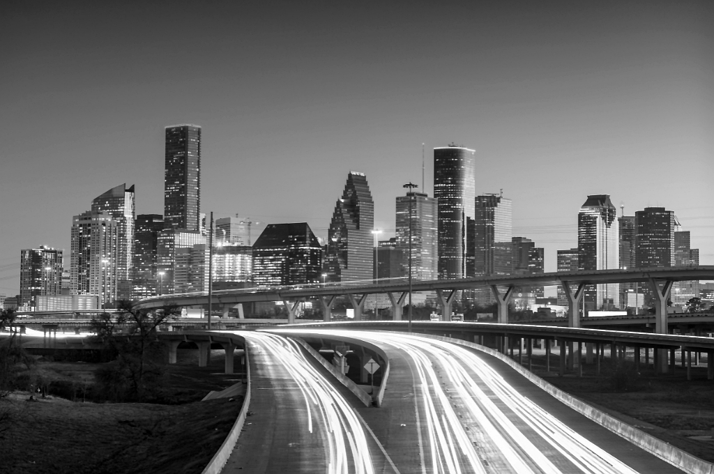 The city skyline of Houston, Texas at dusk. The photo is in grayscale showing a large interstate interchange and the skyscrapers of the city behind it. Reveille Advisors works from Houston to serve our Texas market.