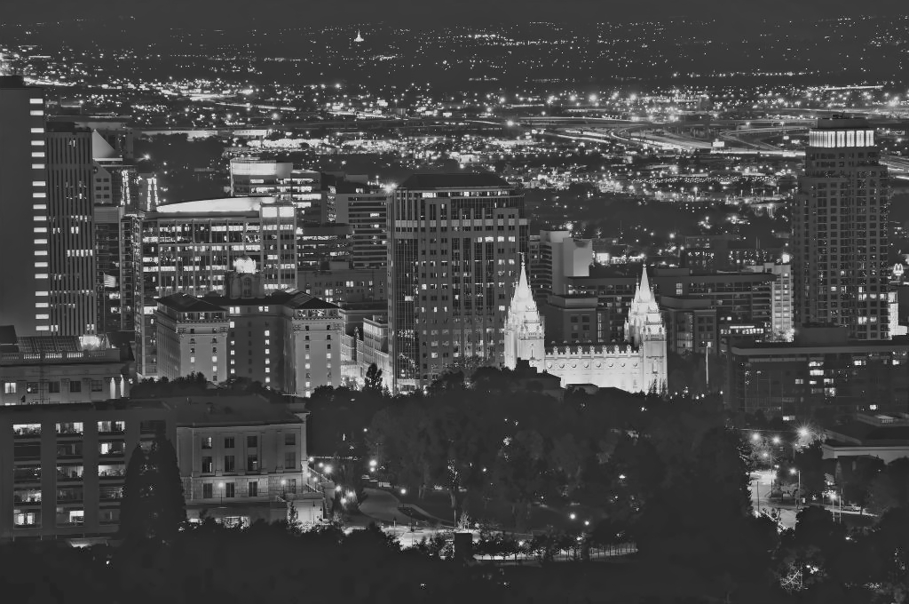 The city skyline of Salt Lake City at night. The photo is in grayscale showing the Mormon Church of SLK highlighted and the skyscrapers of the city behind it. Reveille Advisors works from Salt Lake City to serve our Utah clients.