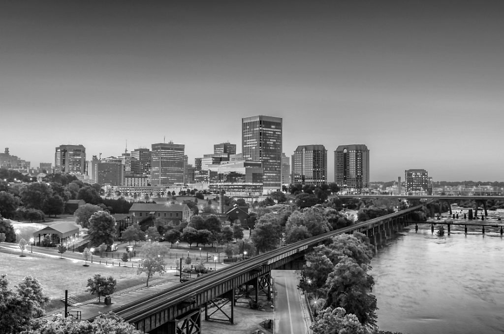 The photo is in grayscale showing the Virginia waterfront and the skyscrapers of the city behind it. Reveille Advisors works from Virginia Beach to serve our Virginia and Beltway clients.