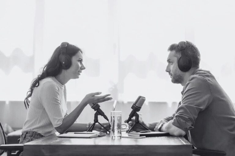 A man and a woman talking on a podcast episode. Looks like they're recording live and in a casual but engaging conversation that they're both enjoying. A great example of Earned Media.