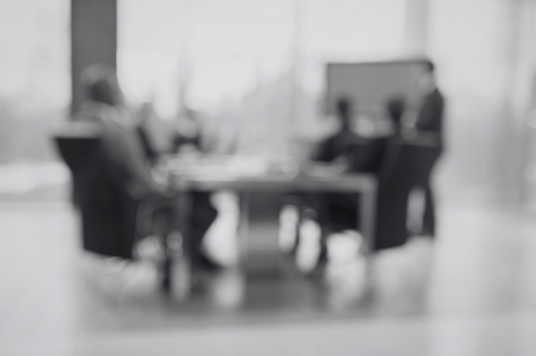 An out of focus photo of a conference room table surrounded by board members behind closed glass doors. It appears they are dealing with crisis management issues, which Reveille Advisors can help clients overcome.