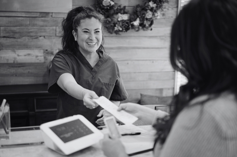 A friendly looking woman returns a customer's receipt and credit card after completing a transaction. Reveille Advisors provides businesses with strategic intelligence to remain competitive.